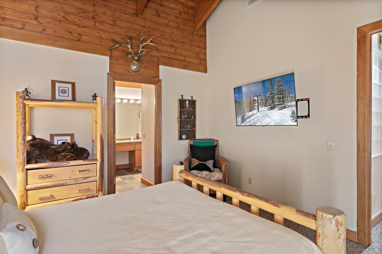This inviting bedroom at 1296 Pinnacle features a wallmounted smart TV and a private ensuite bath — a perfect combination of comfort and convenience.