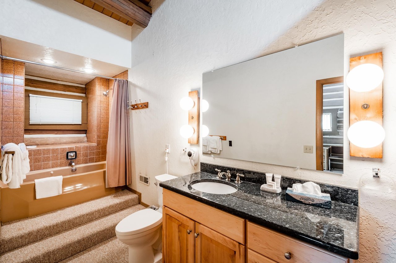 Clean and wellappointed, this full bathroom at Temptation 8 features dark granite countertops, warm wood cabinetry, and a tub and shower combo.