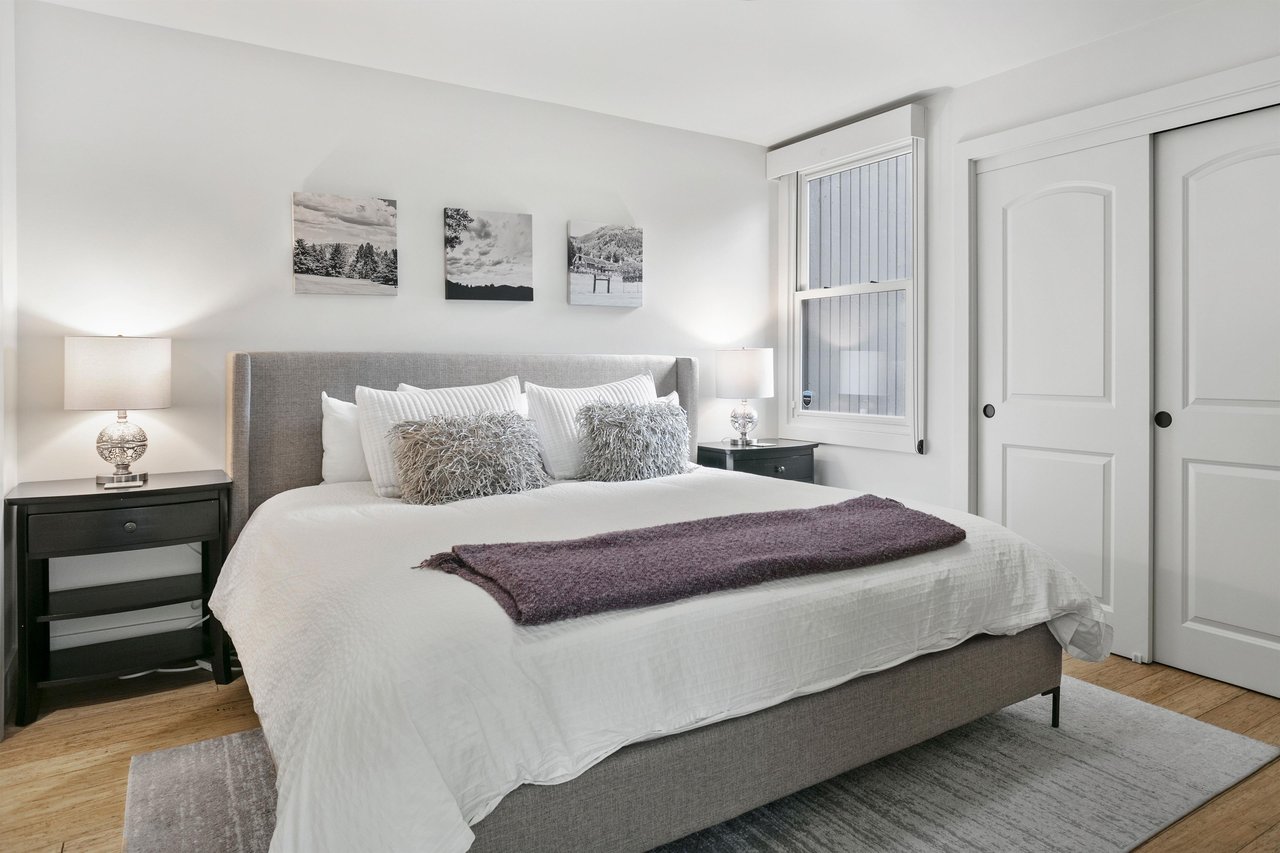 Retreat to the elegantly appointed king bedroom at Three Kings 64, where crisp white bedding, soft neutral tones, and carefully curated mountain artwork create a peaceful and sophisticated sanctuary i