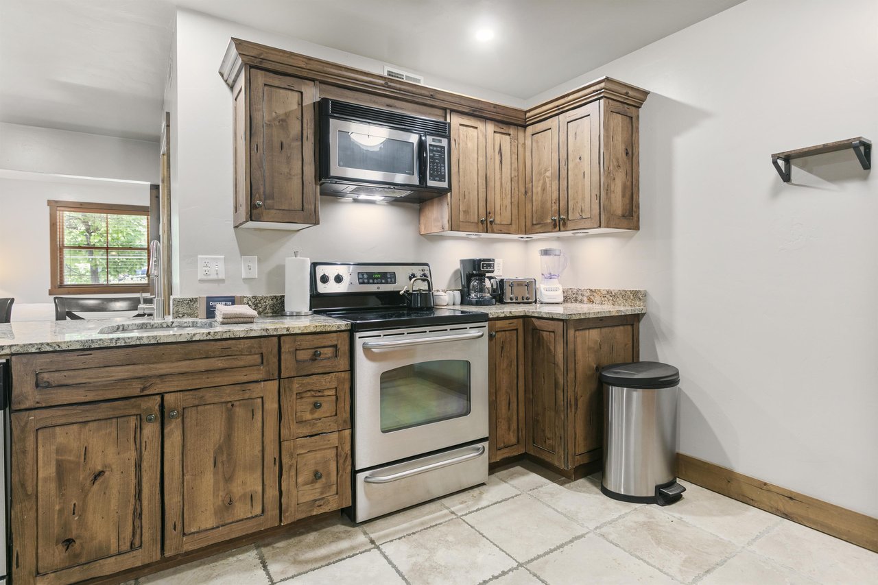 Your fully equipped kitchen features rustic wood cabinetry, granite countertops, and modern appliances including a stove, microwave, and coffee maker—everything you need in the perfect Park City vacat
