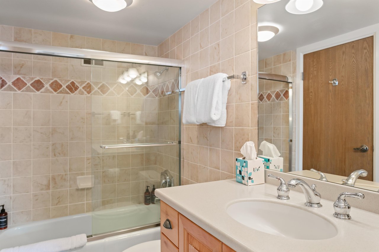 Resort Plaza 5064 continues to impress with a clean and wellappointed bathroom featuring a glassenclosed tub and shower, warm tile accents, and a spacious vanity that add a refreshing touch of comfo
