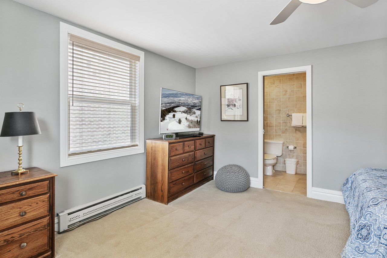 A cozy bedroom nook at Resort Plaza 5064, featuring a rustic wood dresser, an ocean art print, and a peek through to the ensuite bath.
