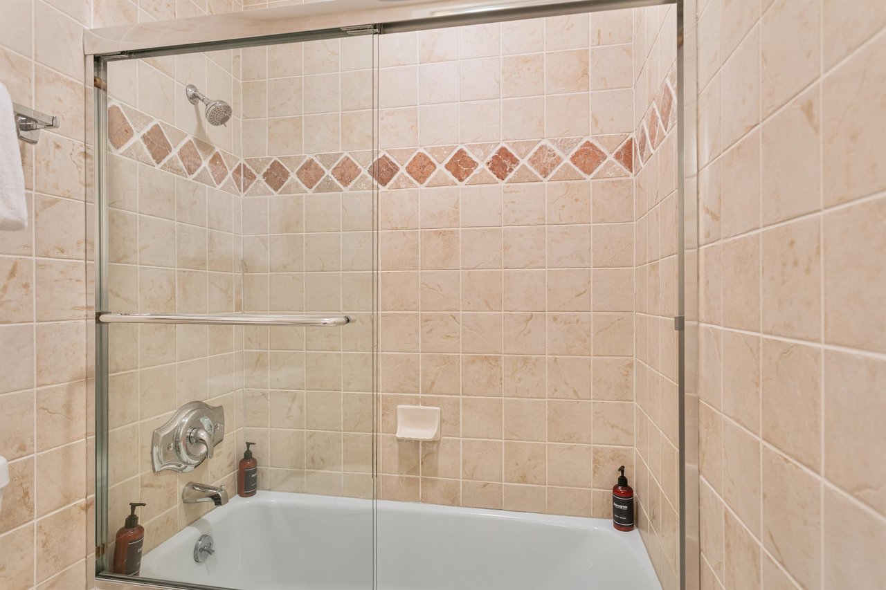 Guest bathroom at Resort Plaza 5064, featuring a deep soaking tub with a sliding glass shower door and classic tile accents.
