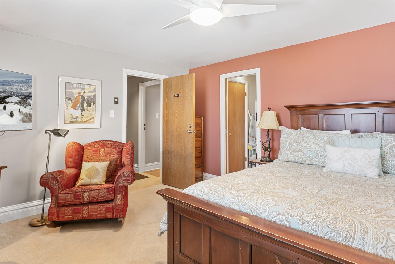 Retire to the spacious and elegantly furnished king bedroom at Resort Plaza 5064, where classic wooden accents, a cozy sitting area, and a wallmounted TV create the perfect sanctuary for a restful ni