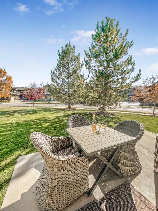 Your private outdoor seating awaits on a spacious patio framed by lush green grass and mature trees, with peaceful neighborhood views stretching beyond—perfect for morning coffee or evening wine.