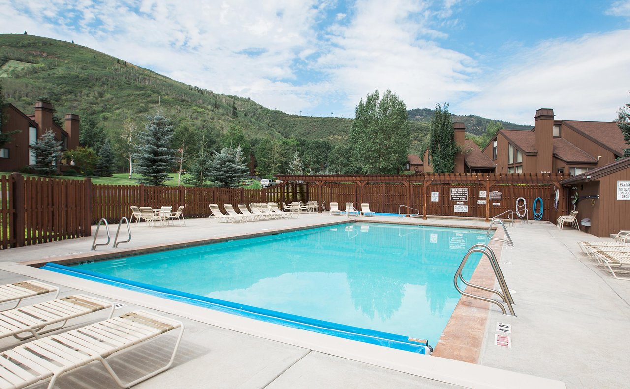 A tranquil outdoor pool surrounded by lush green hills and mountain views, offering a refreshing retreat under open skies in a peaceful alpine setting.