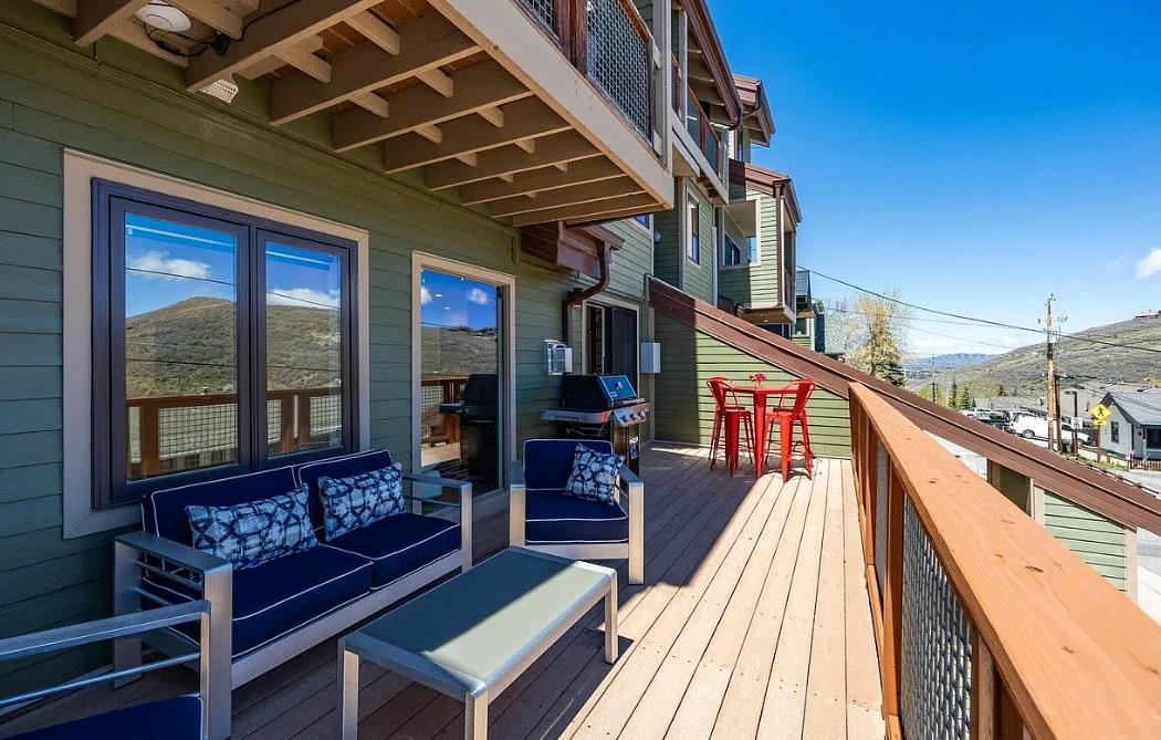 This spacious deck overlooks the surrounding mountains and valley, offering an inviting spot to relax outdoors with comfortable seating, a BBQ grill, and a hightop table for al fresco meals.