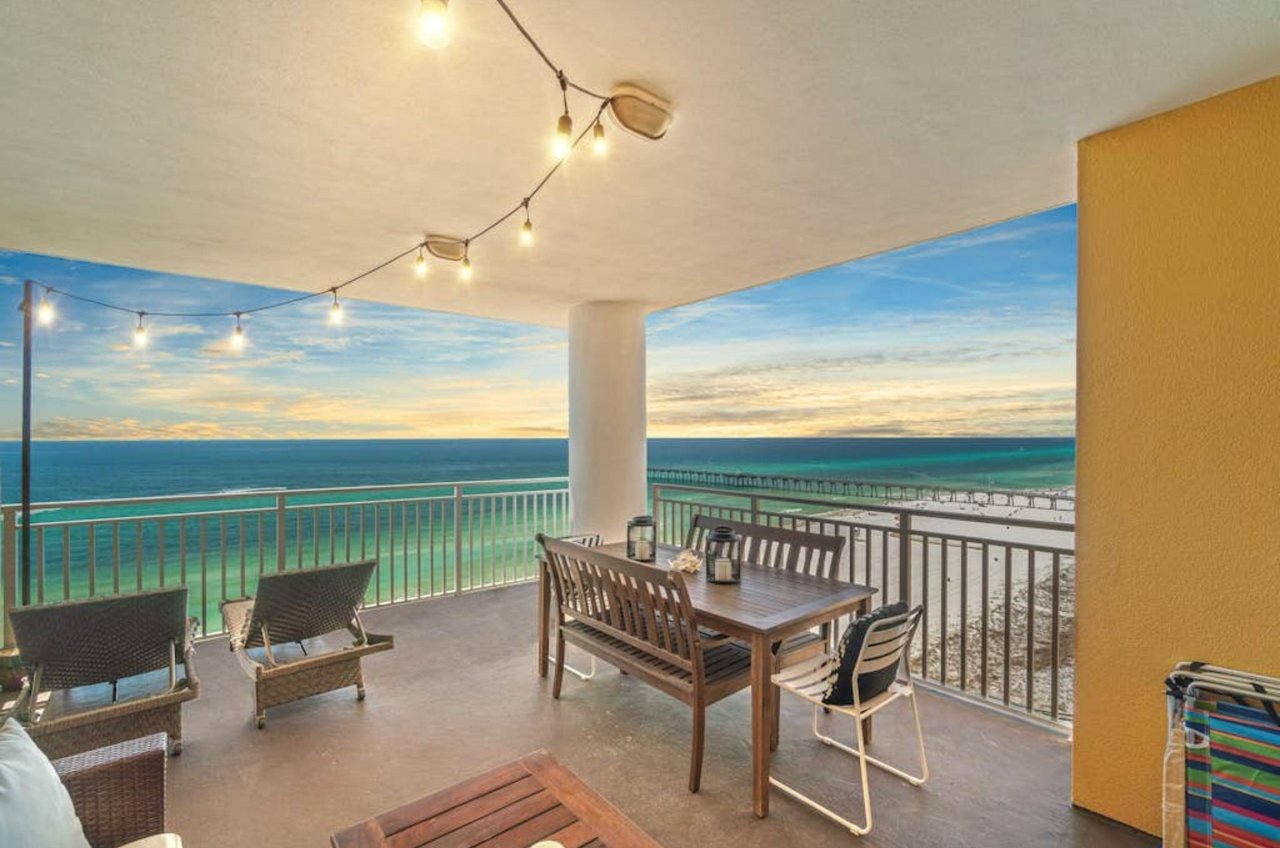 A private balcony with fairy lights a dining table and chairs at Sterling Reef in Panama City Beach Florida