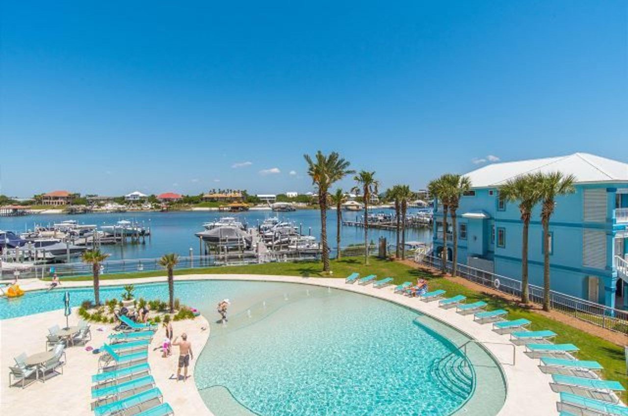 Aerial view of an outdoor pool with lounge chairs next to a marina on the bay