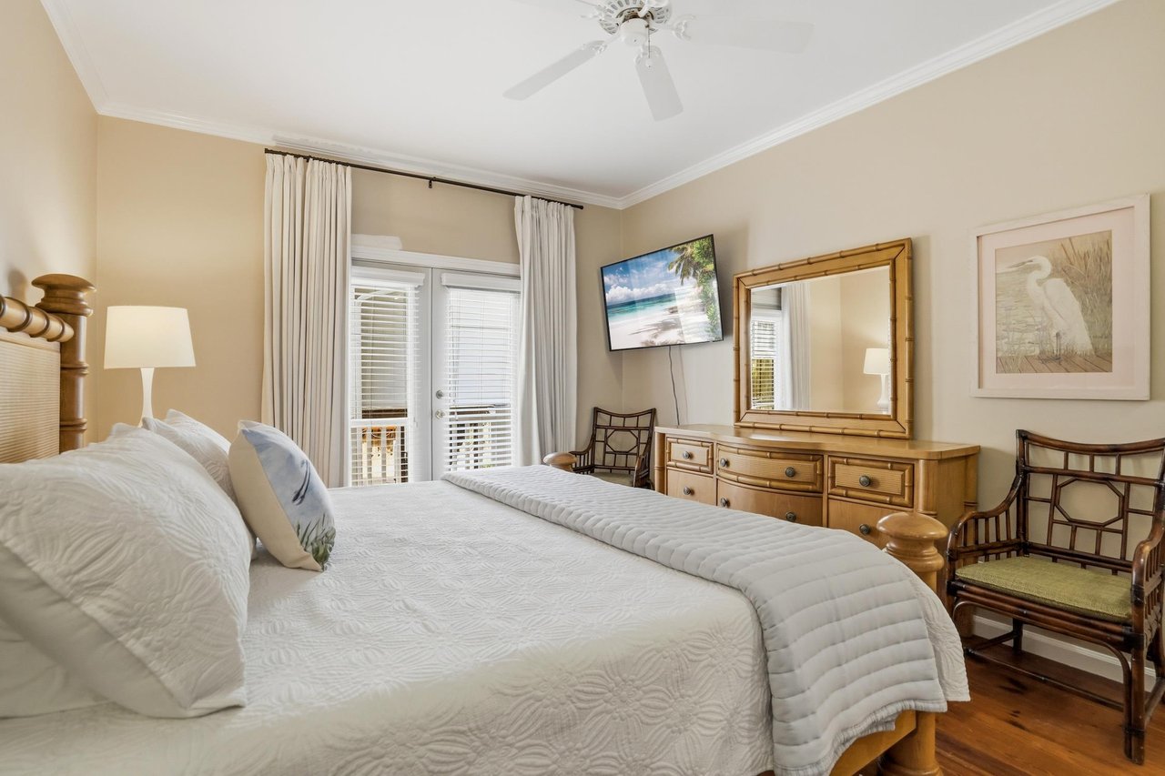 Main floor king primary suite with hardwood floors, mounted TV, and French doors to the covered balcony.