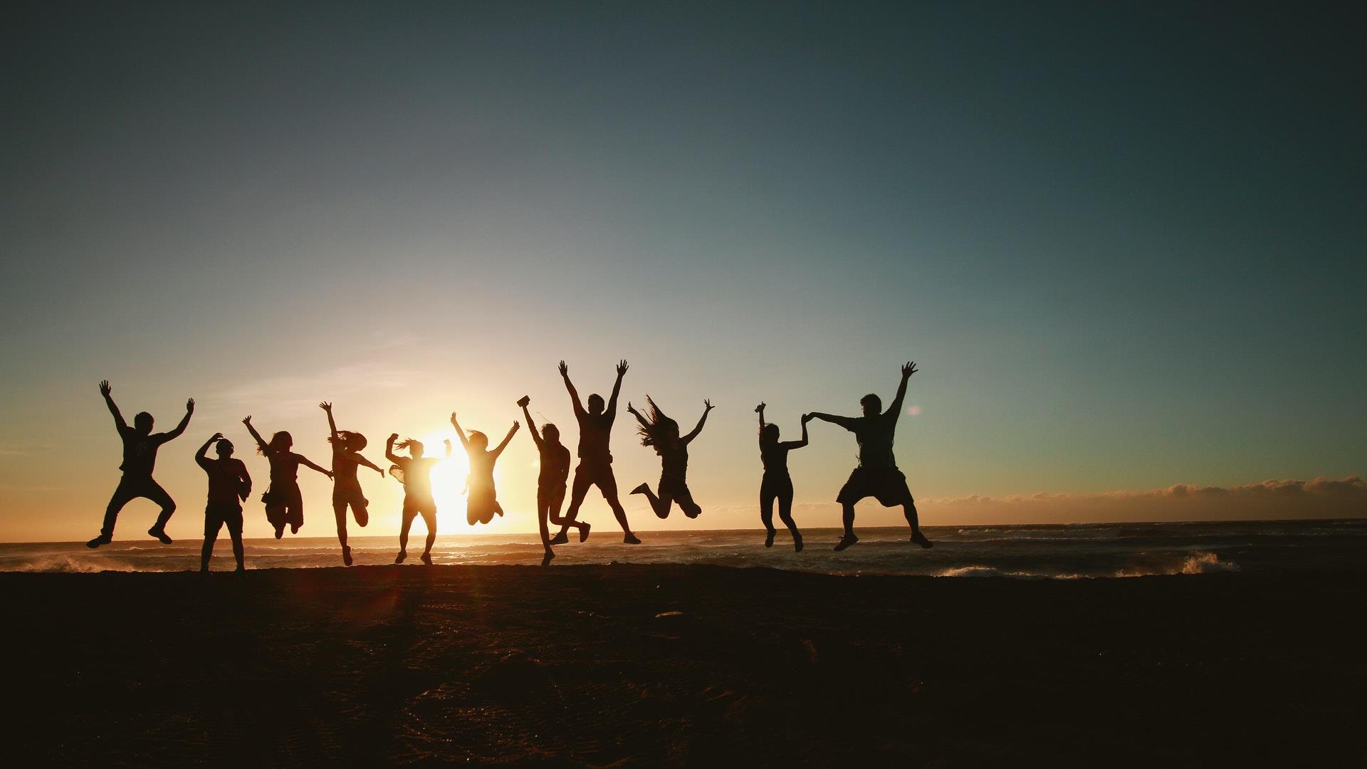 A silhouette of a group of friends jumping together on the beach