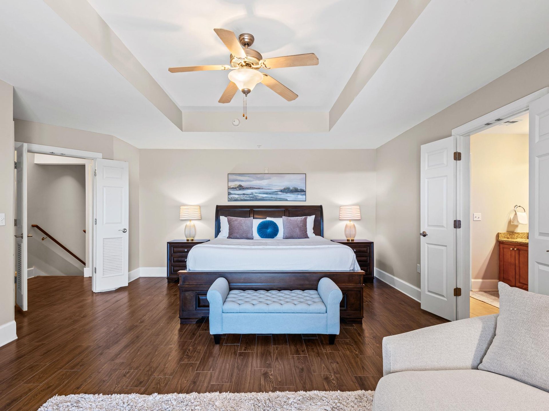 Relax in your spacious primary bedroom featuring a king bed, elegant tray ceiling, and comfortable seating area for the perfect retreat.