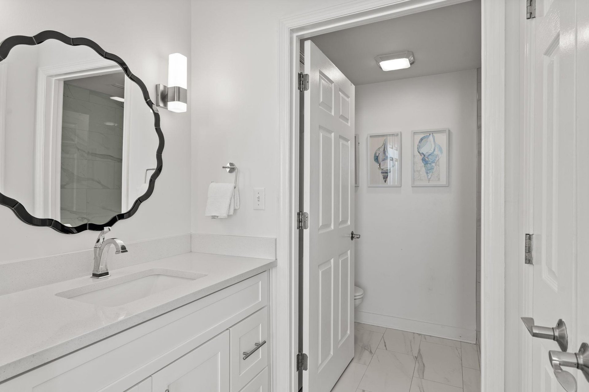 Step into your pristinely clean bathroom featuring elegant marble countertops, stylish scalloped mirror, and thoughtful touches that make your morning routine feel luxurious.