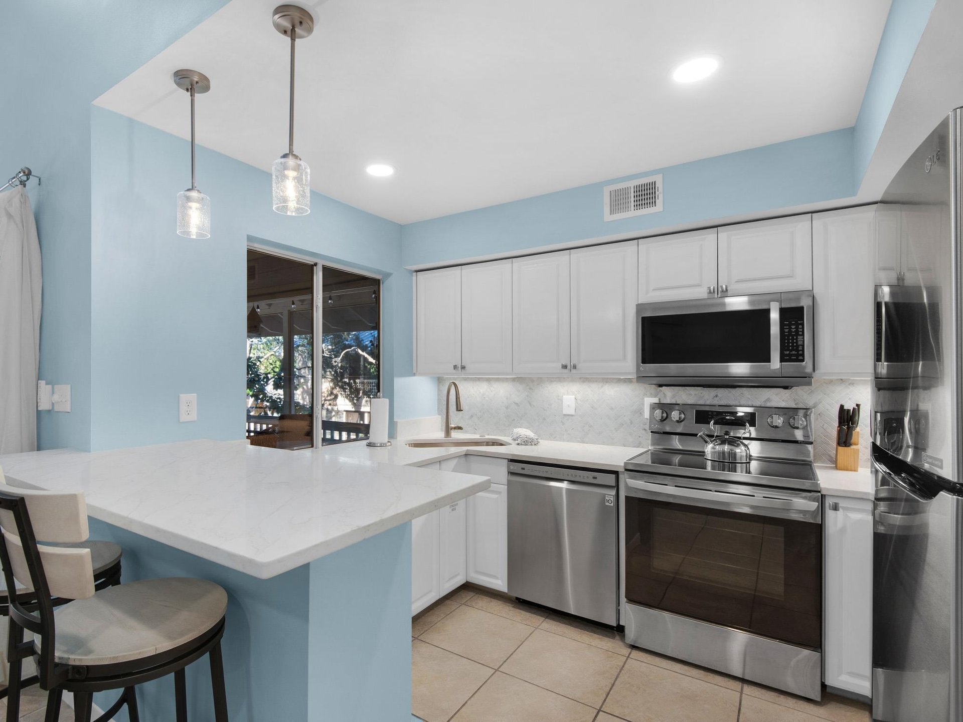 Your modern kitchen invites culinary adventures with gleaming stainless appliances, white quartz counters, and cheerful blue accents that brighten your cooking experience.