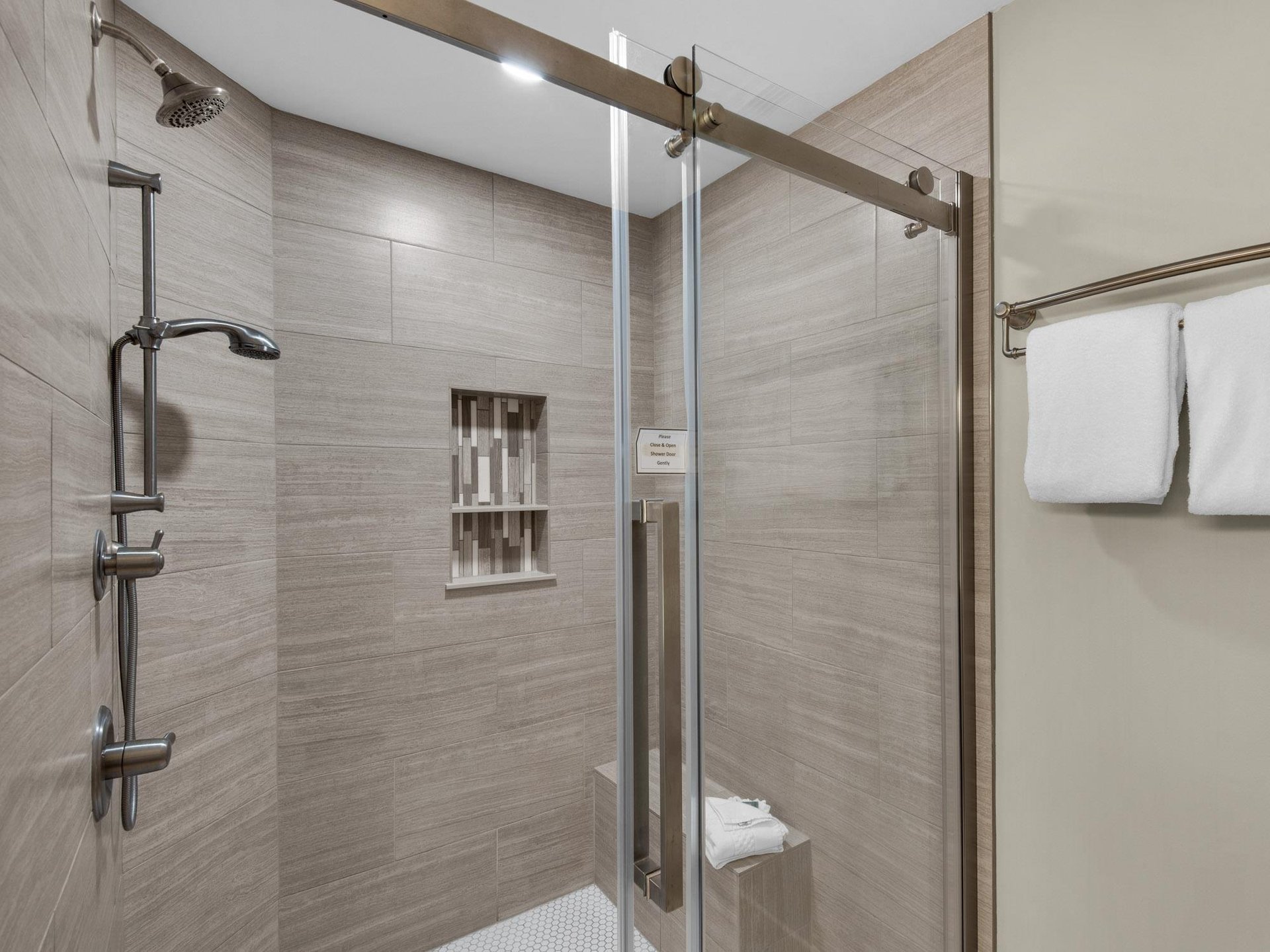 Step into your spacious glassenclosed shower with elegant woodgrain tiles and modern fixtures for your daily refresh.