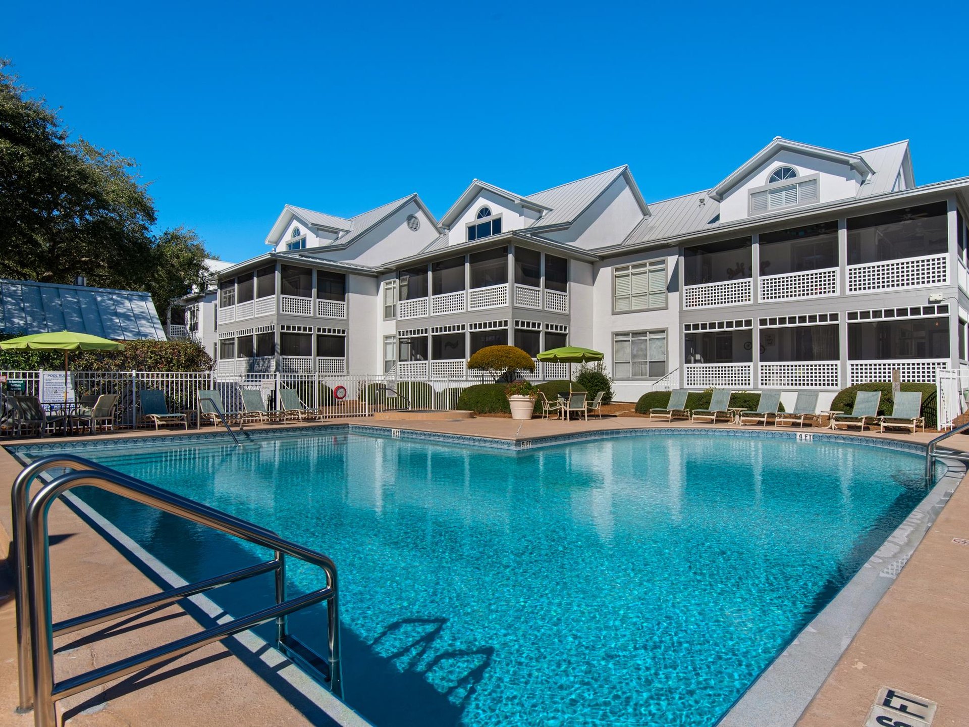 White multistory vacation property with covered balconies and large outdoor swimming pool under clear blue skies.