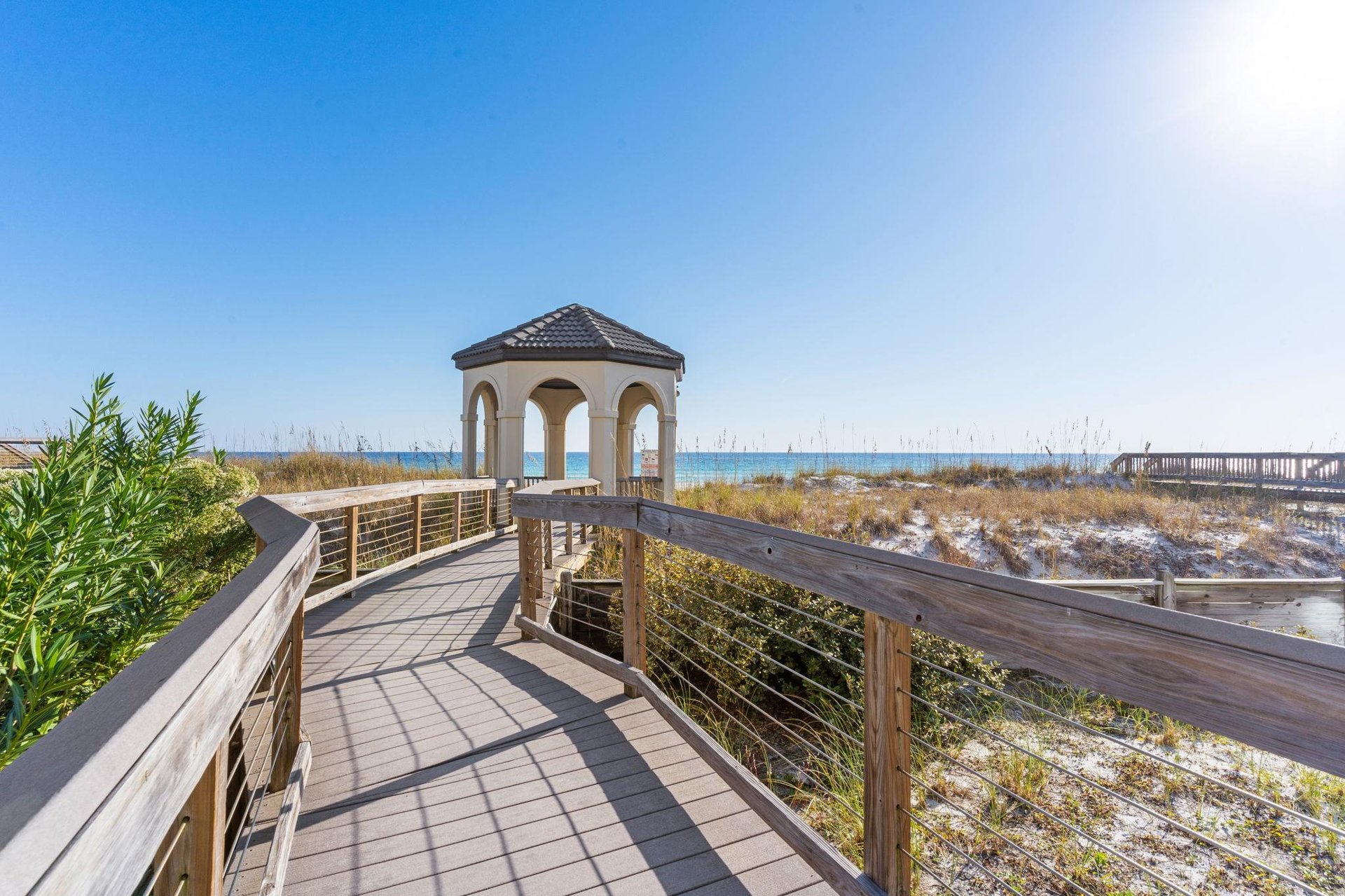 Wooden boardwalk leads to a charming gazebo overlooking pristine beach dunes and ocean views.