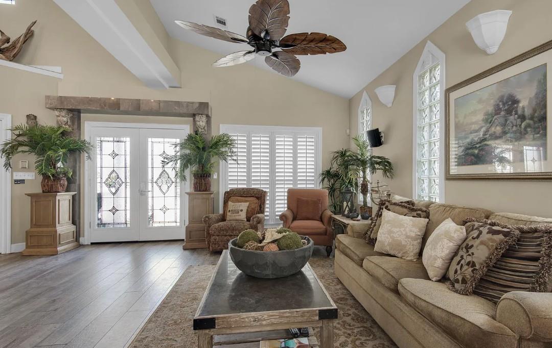 Unwind in this elegant living room with soaring ceilings, tropical ceiling fan, and cozy furnishings perfect for relaxation.