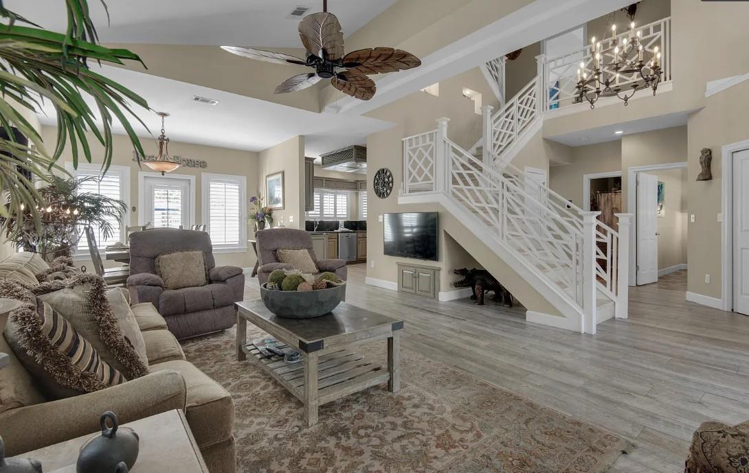 Unwind in your spacious living room with plush seating, tropical ceiling fan, and modern entertainment center beneath elegant stairs.