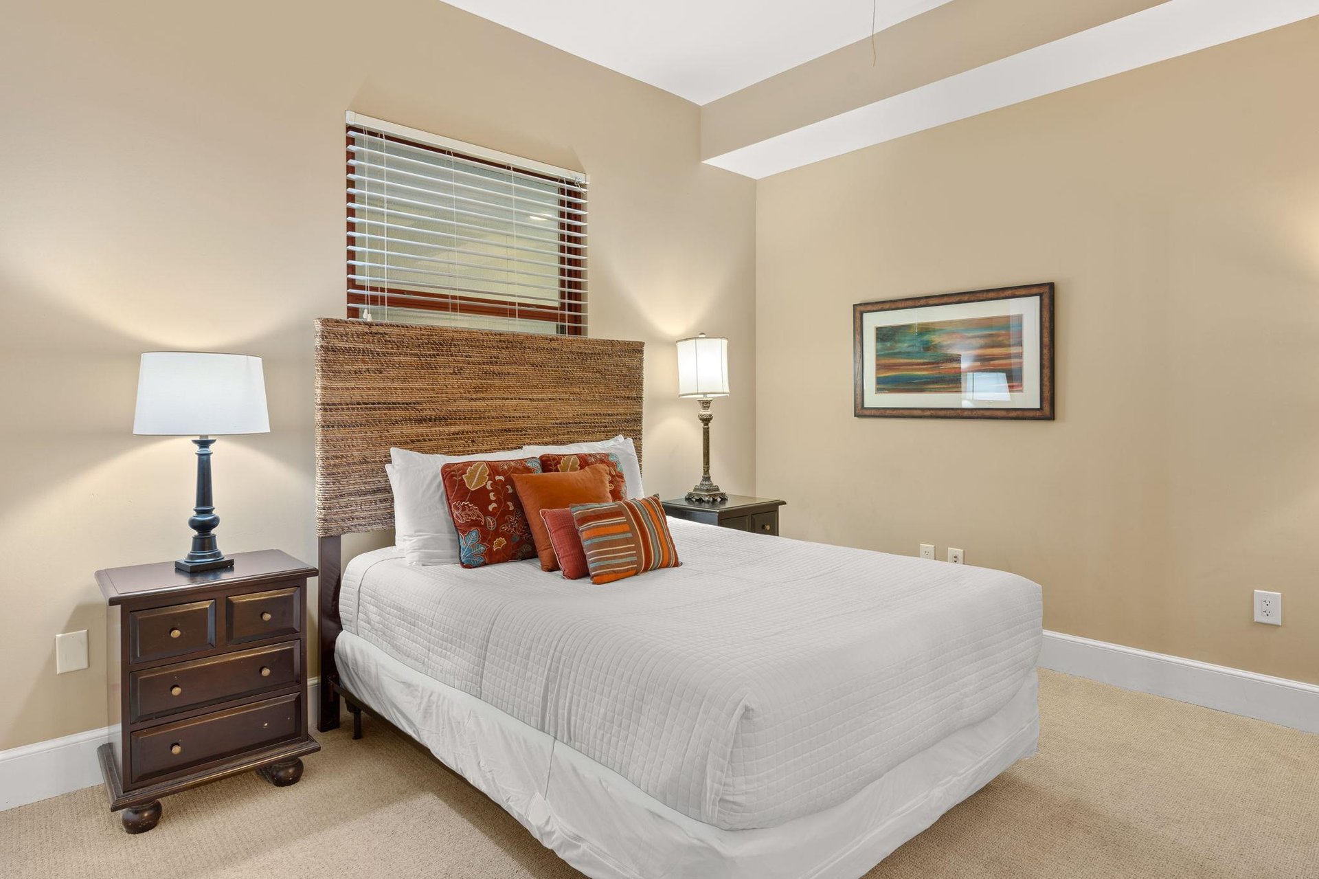 Sink into crisp white linens and colorful accent pillows in your peaceful bedroom retreat with warm lighting and coastal artwork.