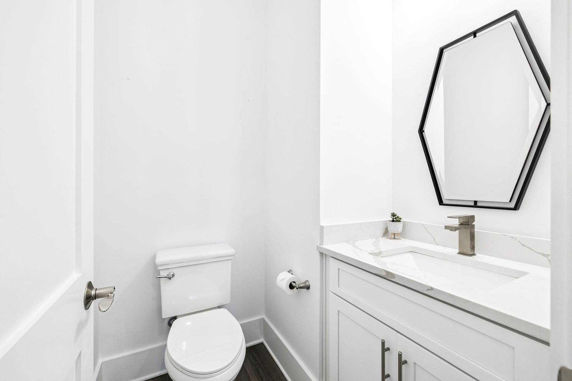 Your elegant powder room features marble countertops, modern fixtures, and a striking geometric mirror for your convenience.