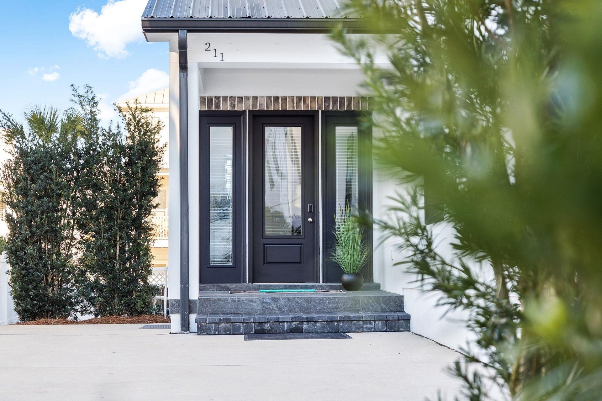 Modern entrance to property 211 with sleek glass doors and tropical landscaping creating an inviting arrival experience.
