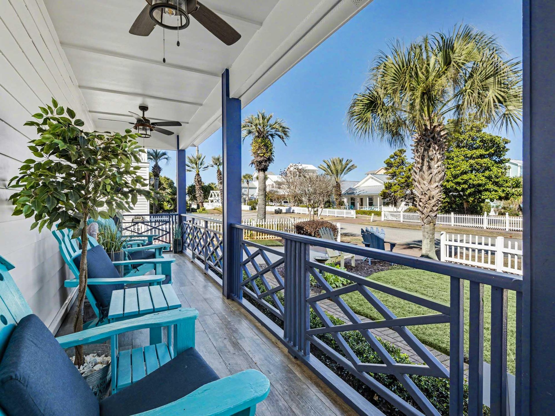 Relax on your private covered balcony with turquoise chairs overlooking lush palm trees and the charming neighborhood—your perfect retreat.