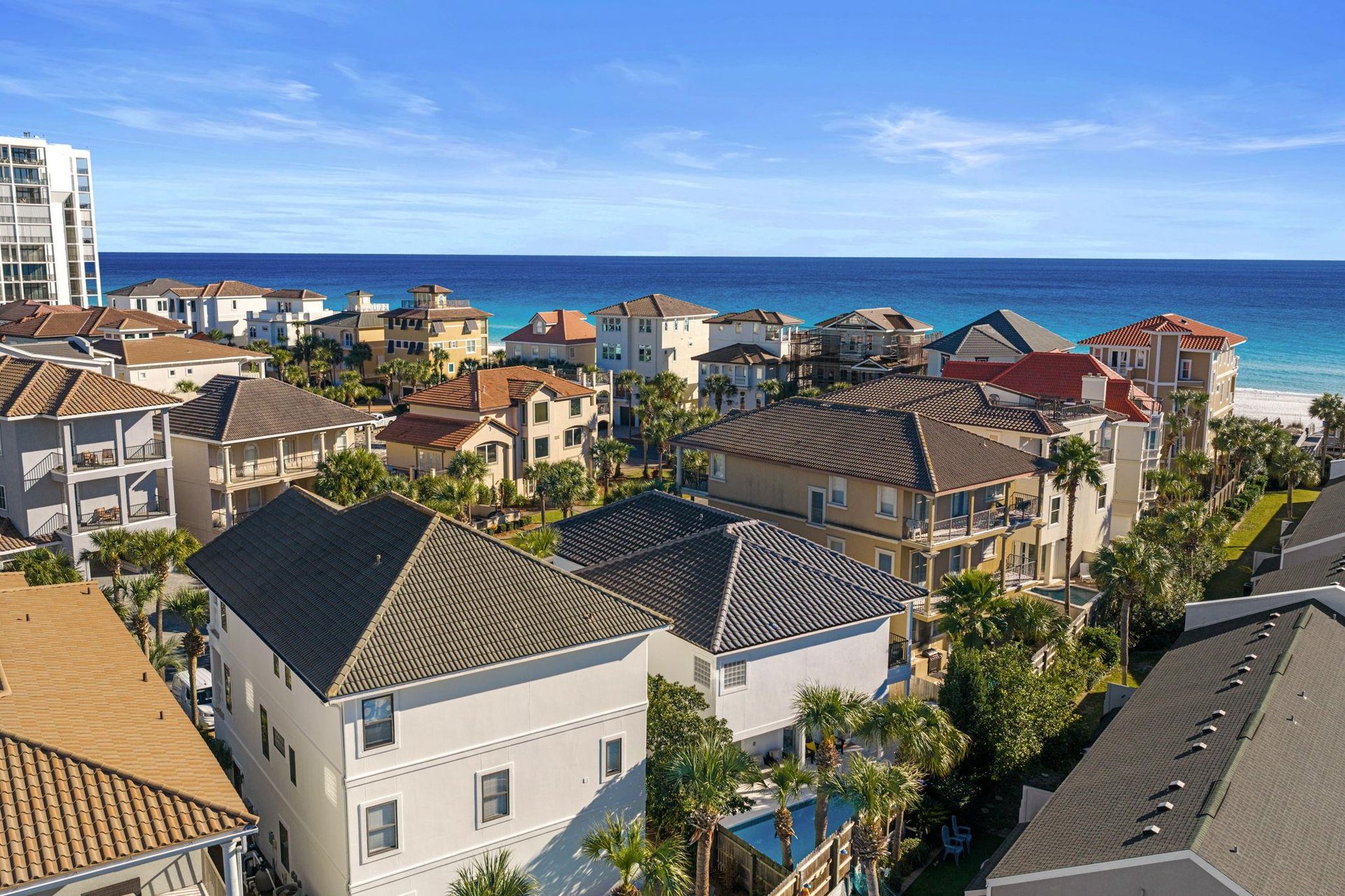 Coastal community overlooking pristine turquoise waters and white sand beaches, surrounded by tropical palm trees and residential buildings.