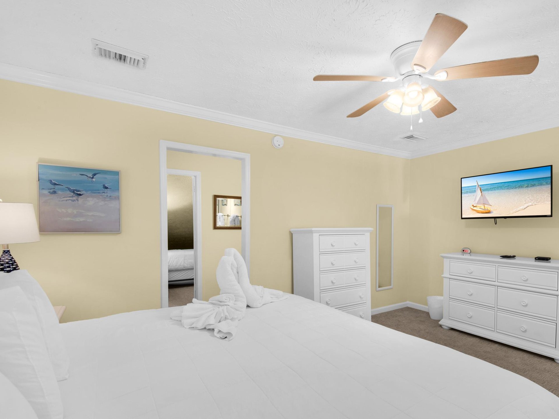 Relax in your peaceful bedroom with crisp white linens, ceiling fan, and calming coastal artwork creating the perfect retreat.