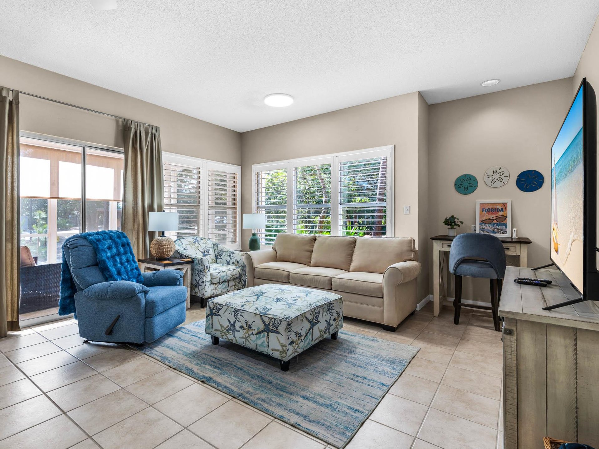 Sink into plush sofas and unwind in the bright living space with coastal blues and natural light streaming through shuttered windows.