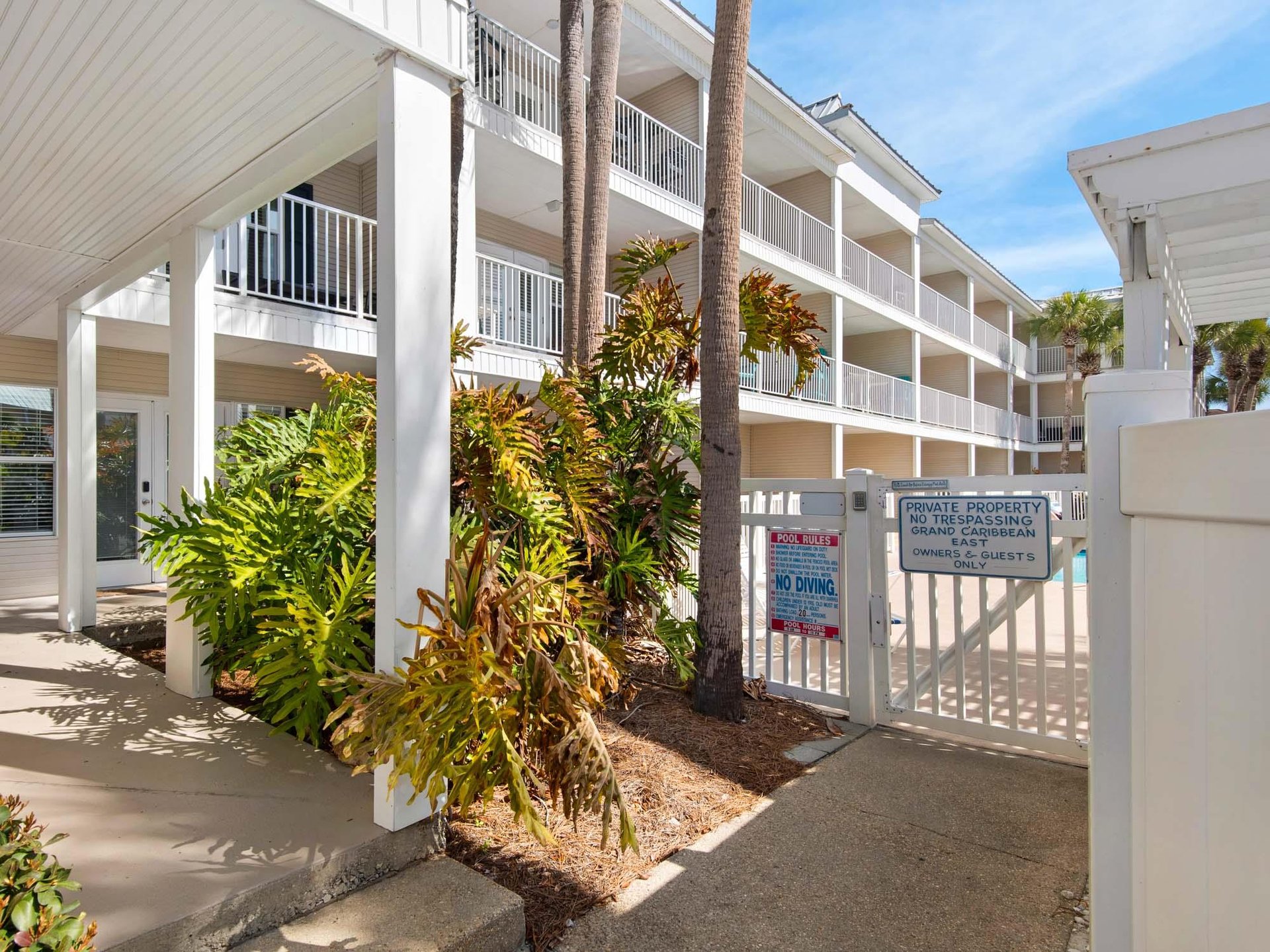 Tropical Caribbeanstyle property featuring white buildings with balconies surrounded by lush palm trees and colorful foliage.