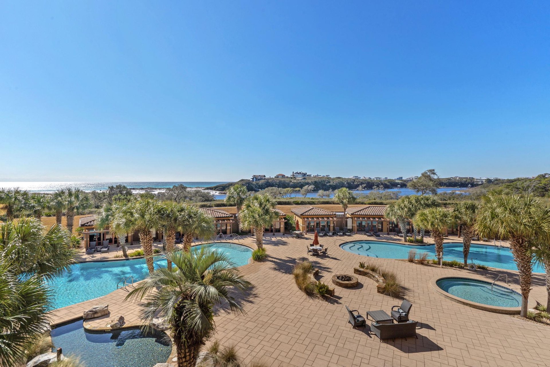 Spacious pool area featuring multiple swimming pools, hot tubs, and lush tropical landscaping with coastal views beyond.