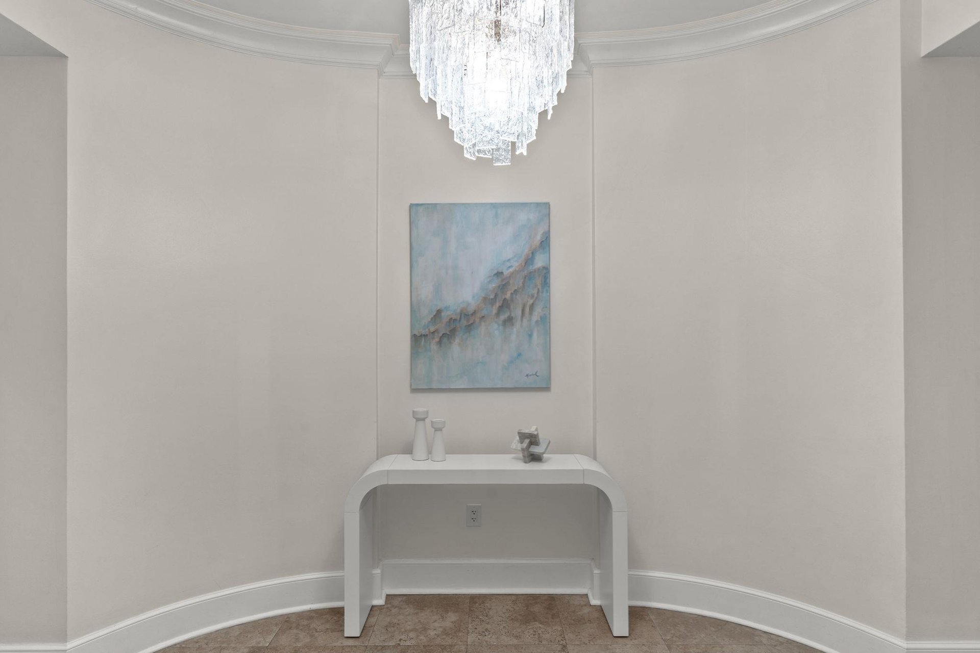 Your elegant foyer welcomes you with a stunning crystal chandelier casting warm light over a sleek console table beneath beautiful artwork.