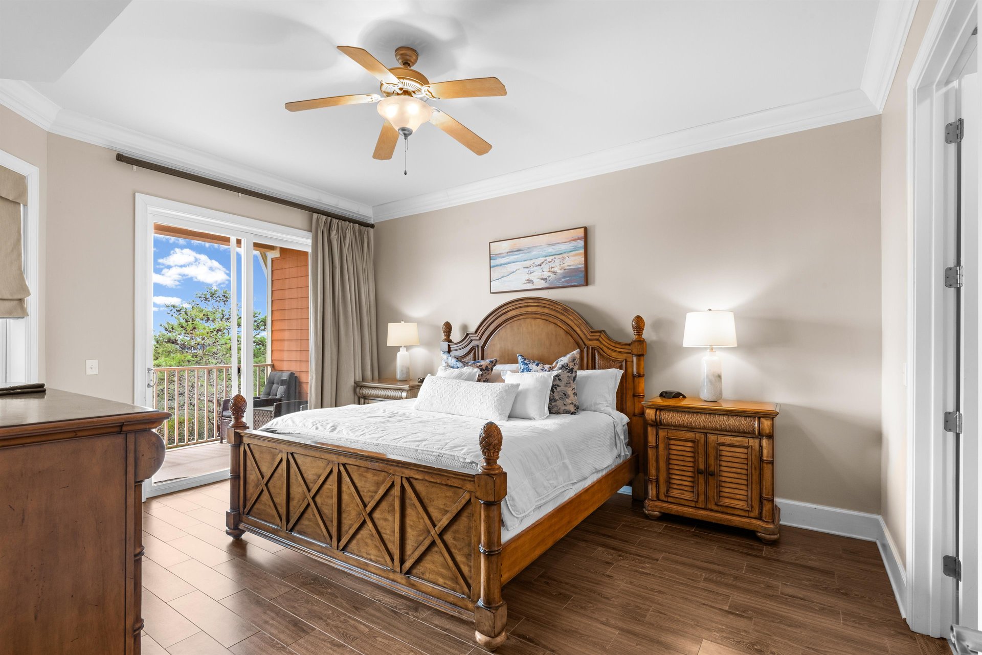 First floor king bedroom with tropical wood furnishings, ceiling fan, and private balcony overlooking lush landscaping.