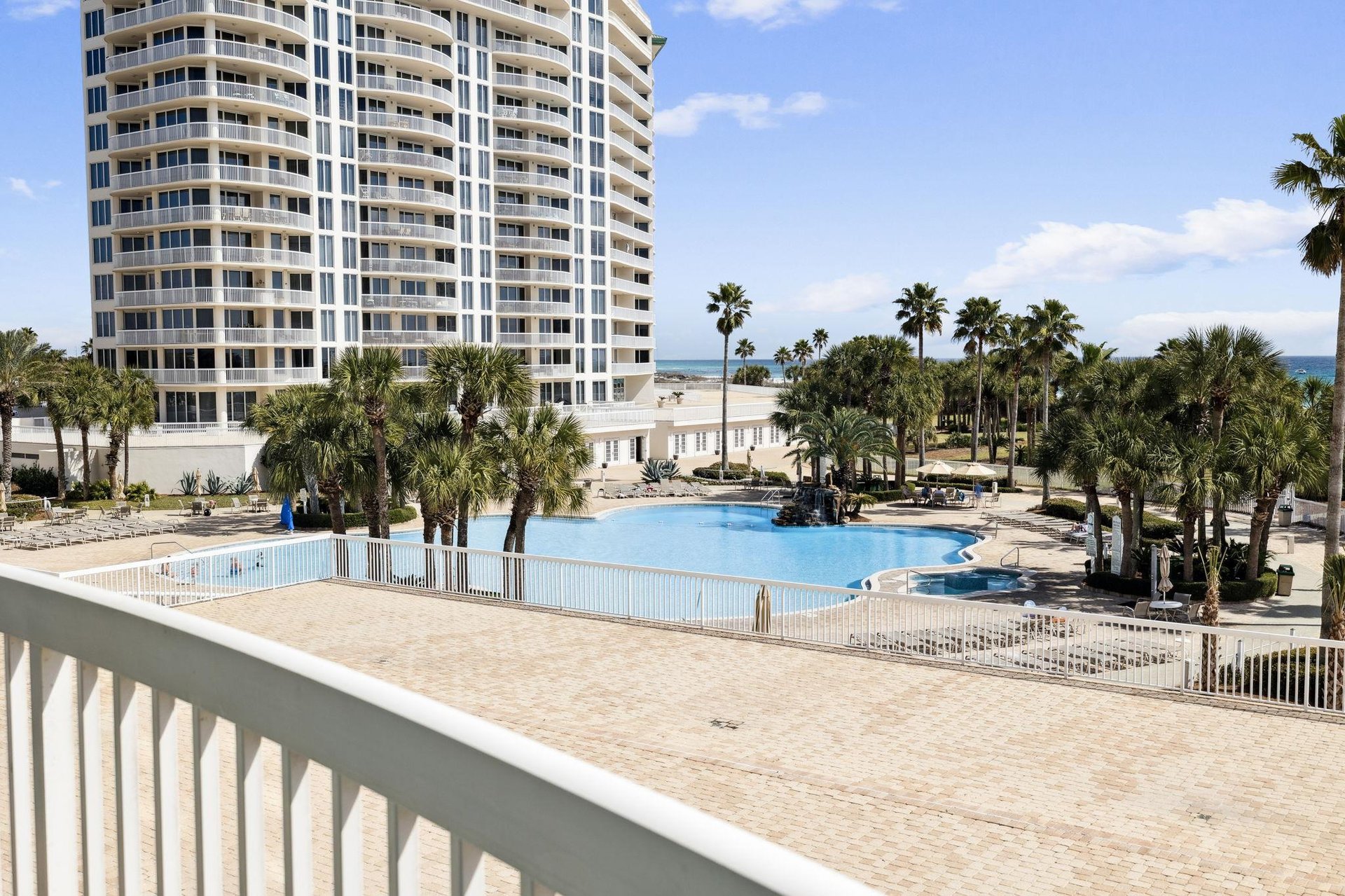 Modern beachfront resort with sparkling pool surrounded by tropical palms and ocean views.
