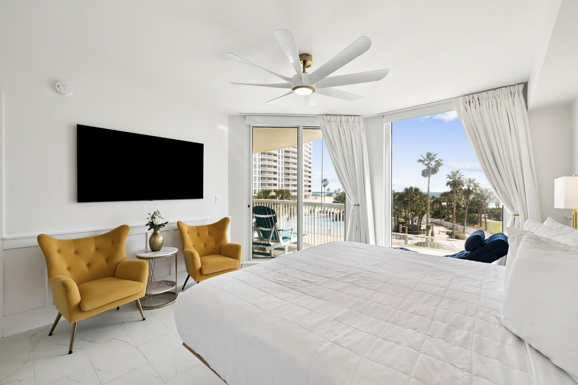 Sink into your plush bed while enjoying pool views from your private balcony. Golden accent chairs and a large TV create the perfect retreat.