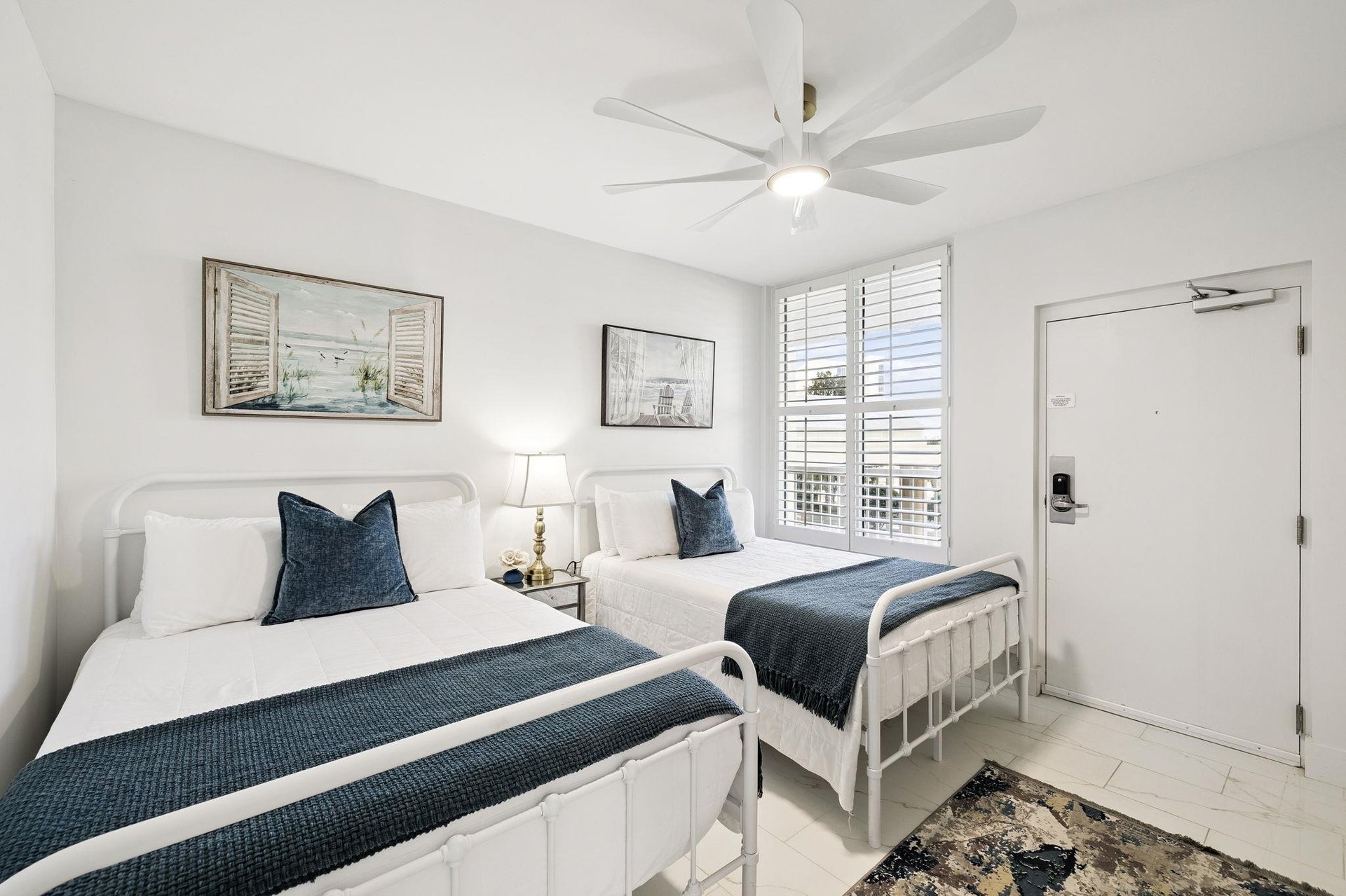 Your peaceful twin bedroom features crisp white linens with navy accents, a ceiling fan for comfort, and coastal artwork creating a serene retreat.