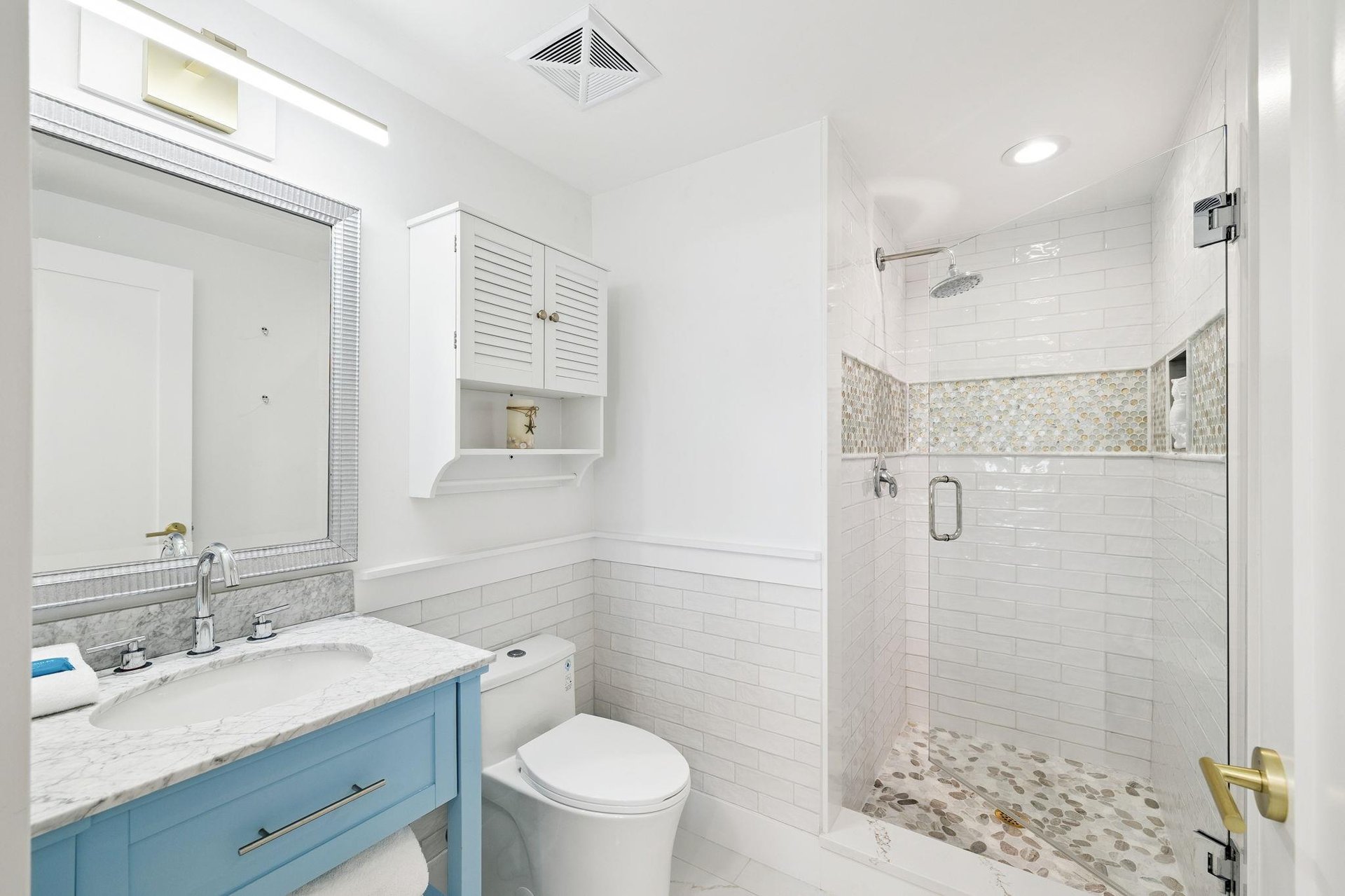 Refresh in your spainspired bathroom with marble counters, rainfall shower, and coastalchic blue vanity.