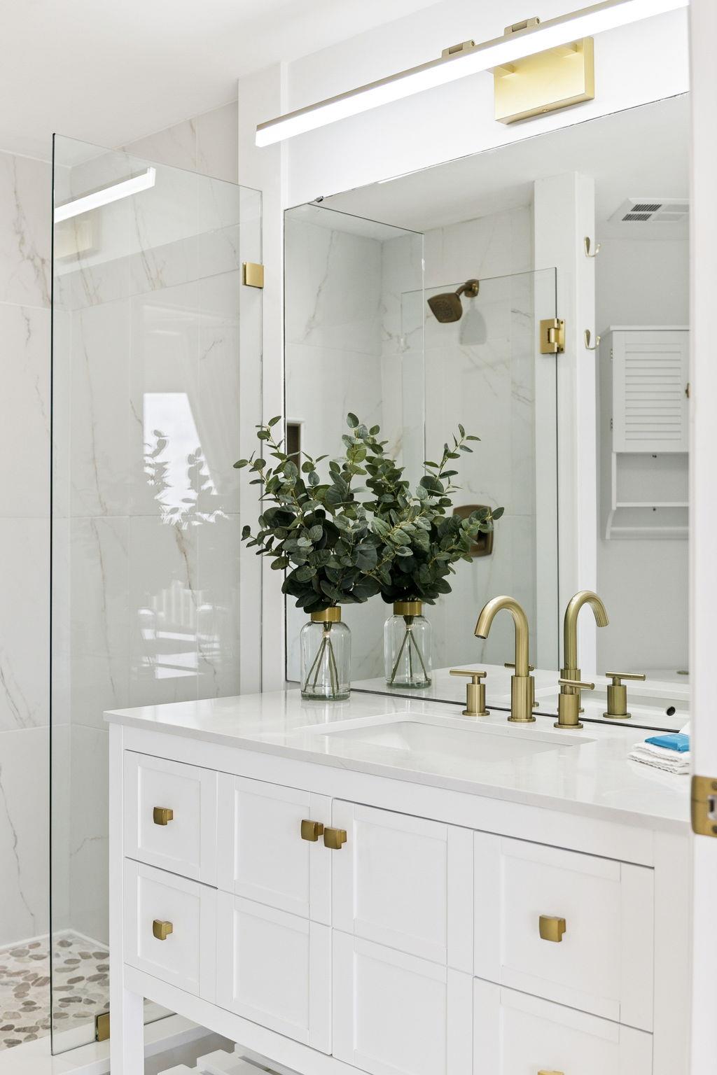 Pamper yourself in this elegant marble bathroom with brass fixtures, fresh eucalyptus, and a luxurious glassenclosed shower.