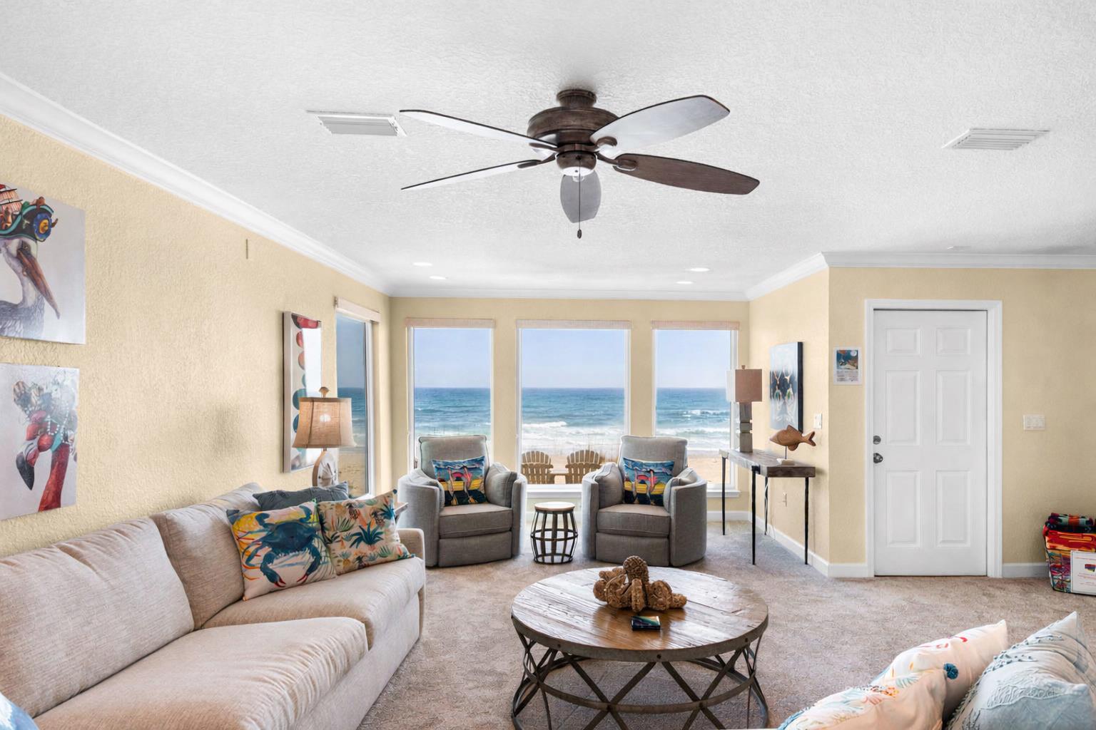 Your beachfront living room captures endless Gulf views through floortoceiling windows, where gentle ceiling fan breezes complement the coastal décor.