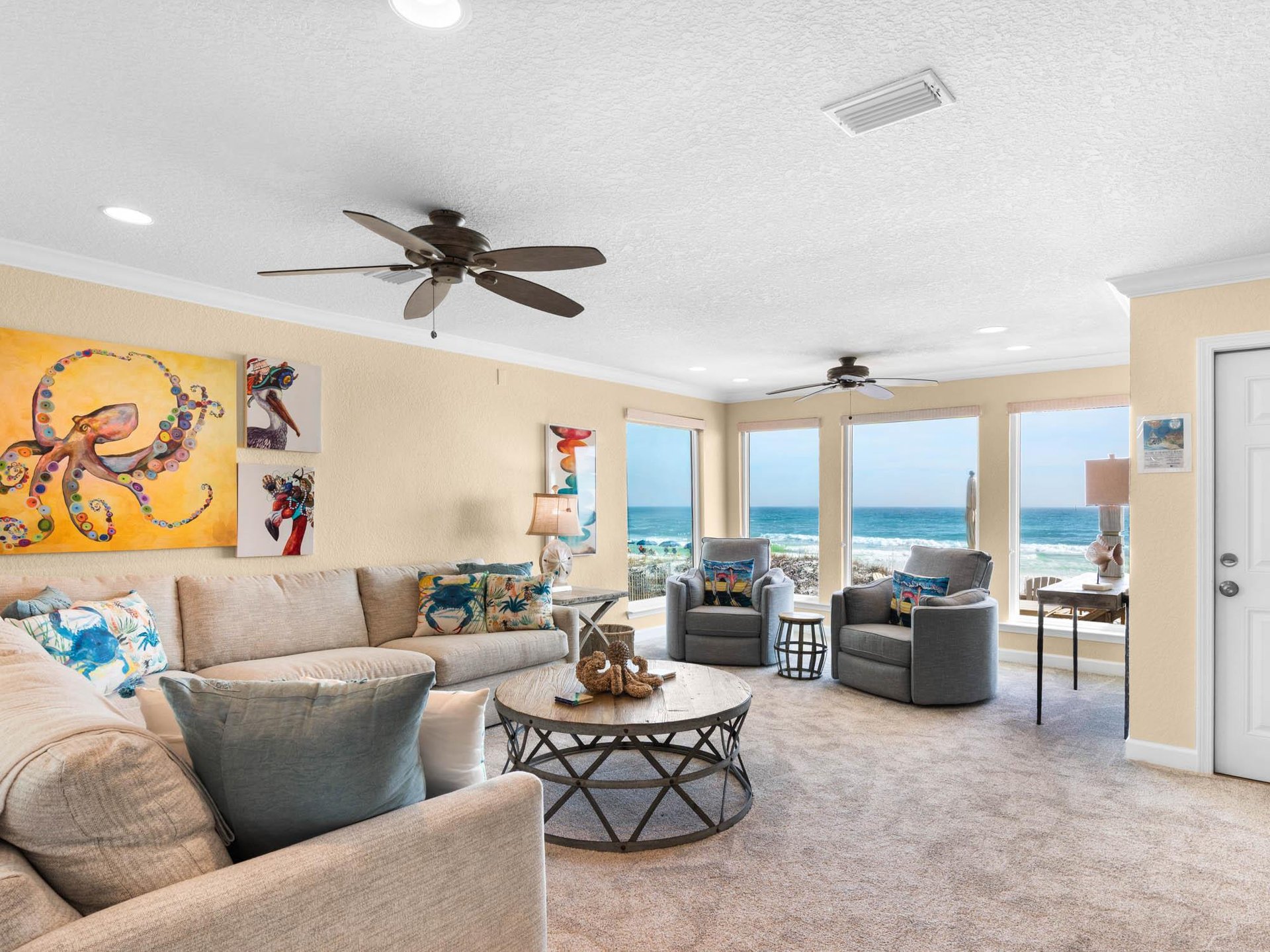 Relax in your Gulfview living room with vibrant art, comfy seating, and endless sea views through panoramic windows.