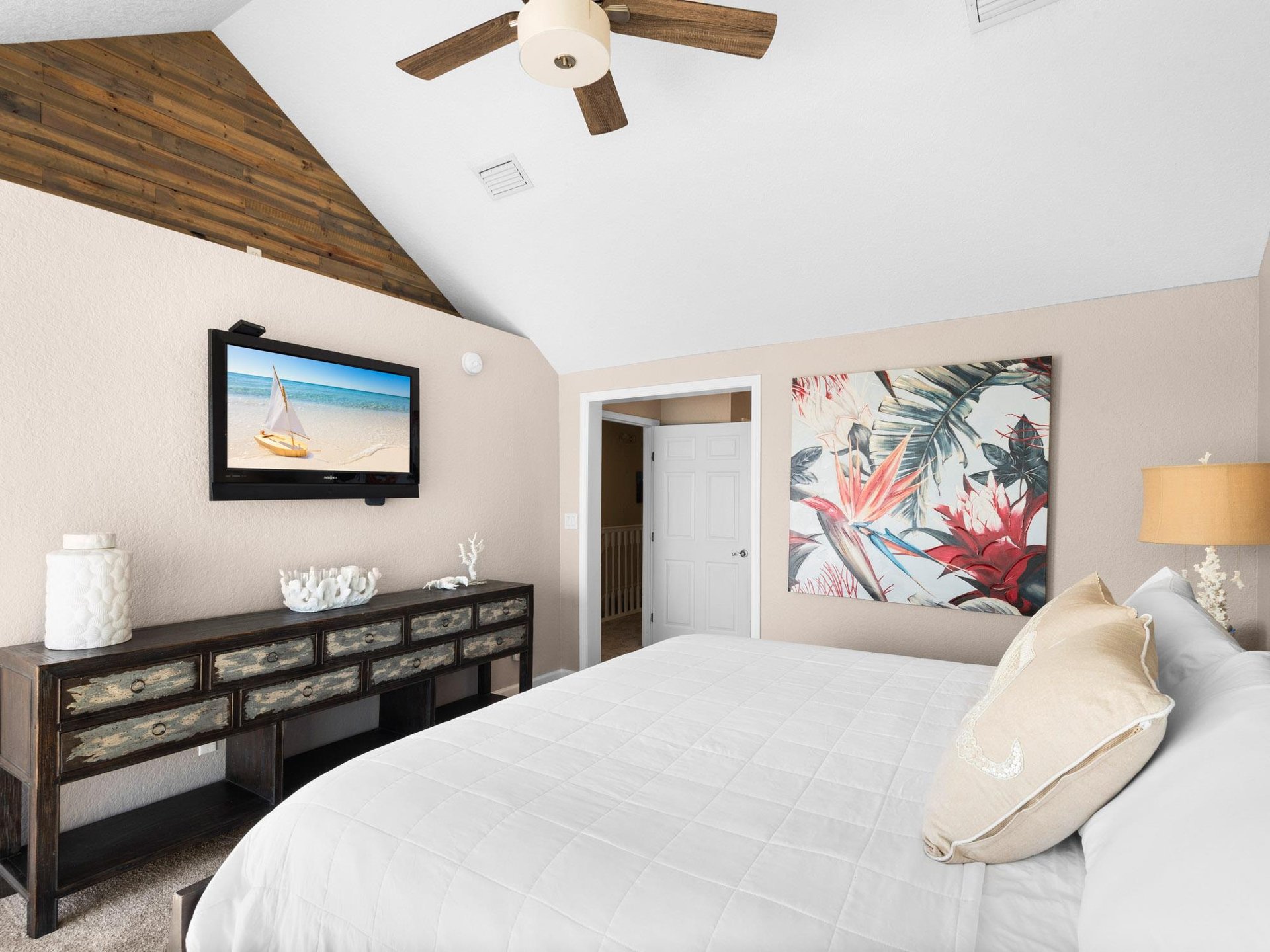 Drift into coastal dreams in the serene primary bedroom, featuring a plush king bed, tropical artwork, and rustic wood accents that create the perfect retreat.