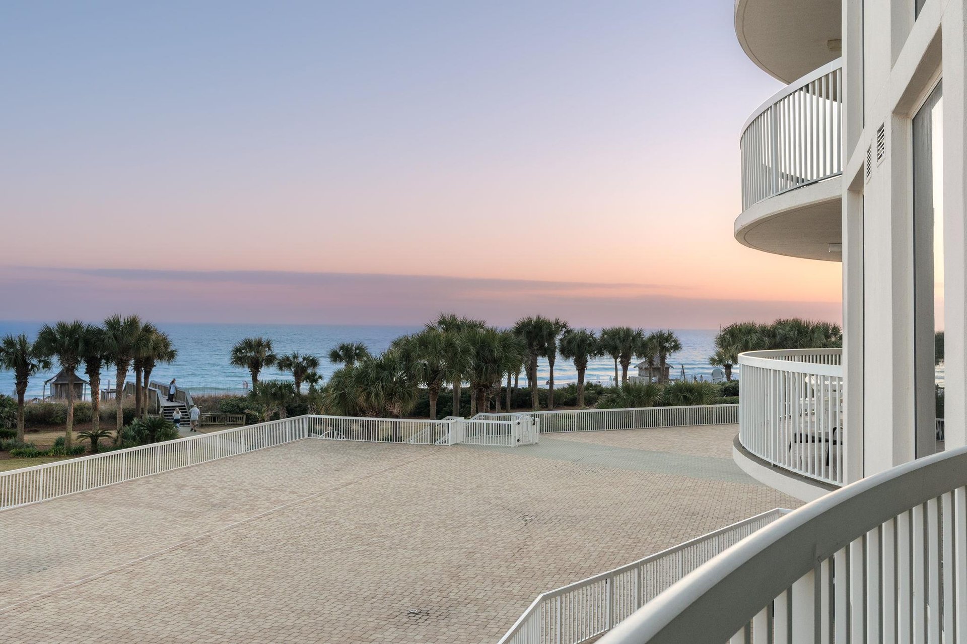 Breathtaking oceanfront balcony with panoramic sea views and stunning sunset skies over swaying palm trees.