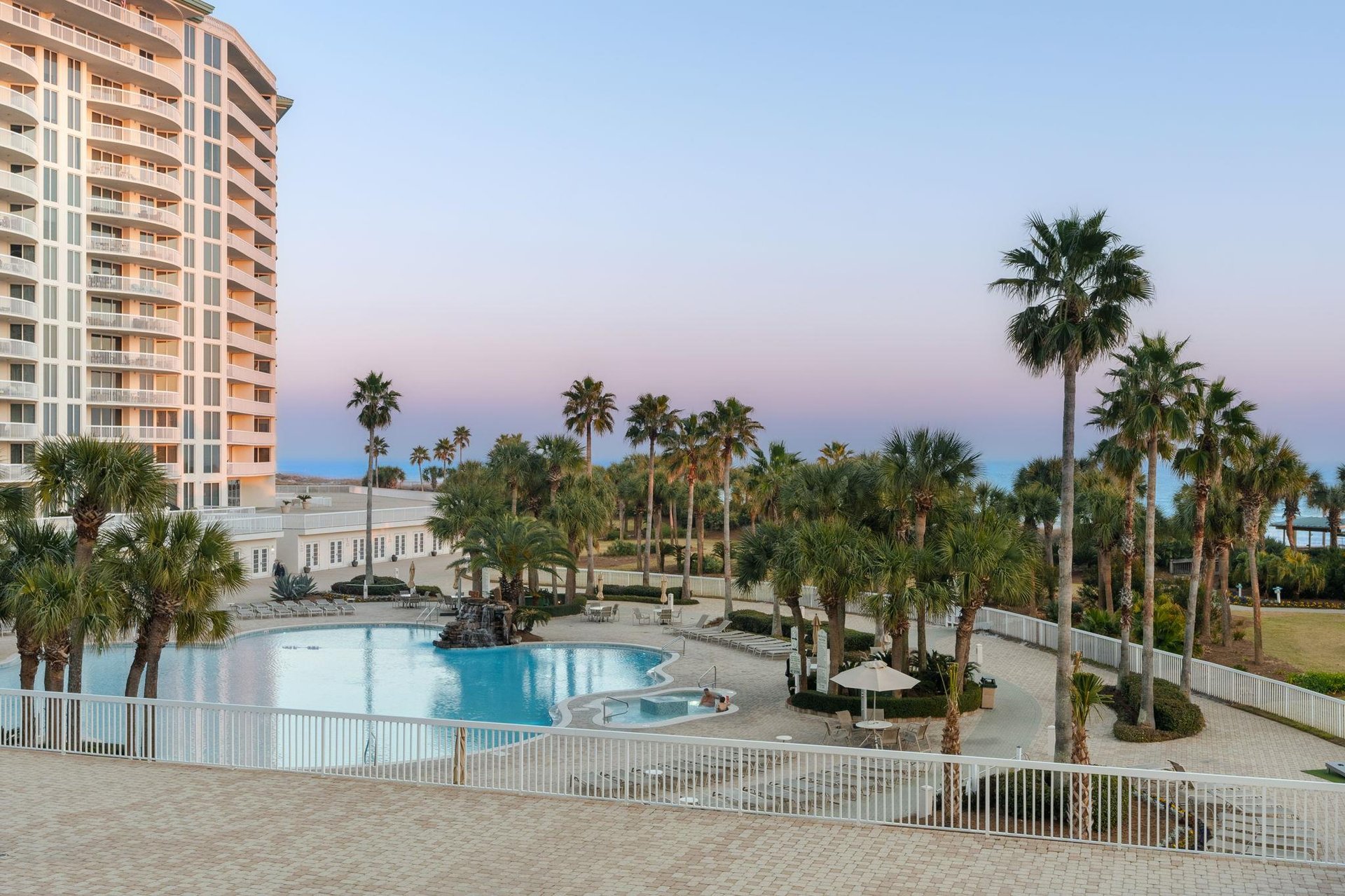 Elegant resort towers rise above tropical palms surrounding a pristine pool deck at twilight.
