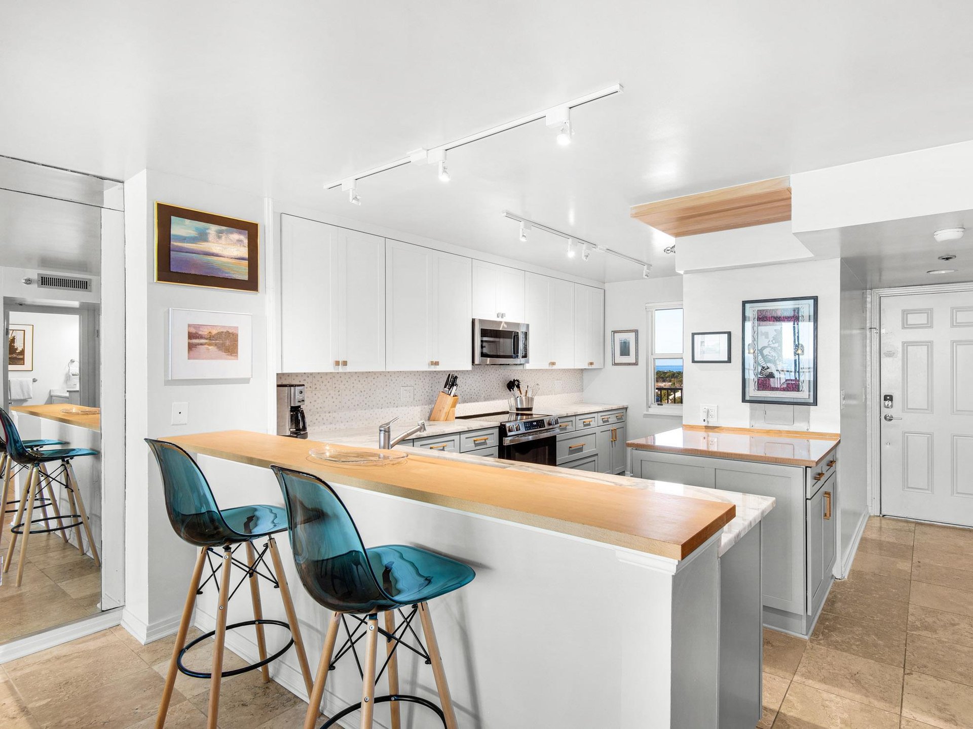 The modern kitchen features sleek white cabinets, warm wood countertops, and stylish turquoise bar seating