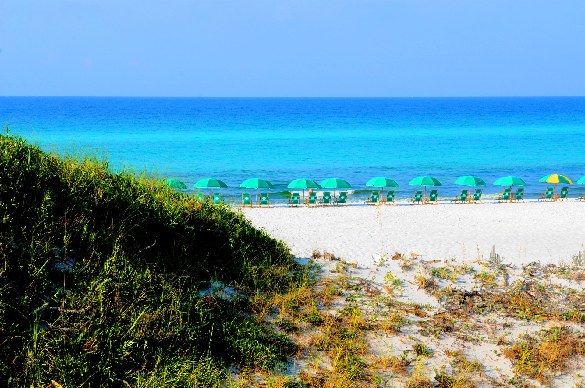 Pristine beach with white sand and turquoise waters, dotted with green umbrellas and beach chairs for perfect relaxation.