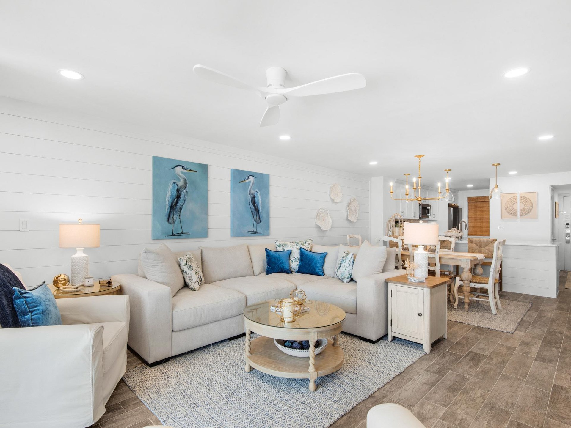 Relax in your bright, coastalinspired living space featuring plush sectional seating, charming heron artwork, and an open layout flowing into the dining area.