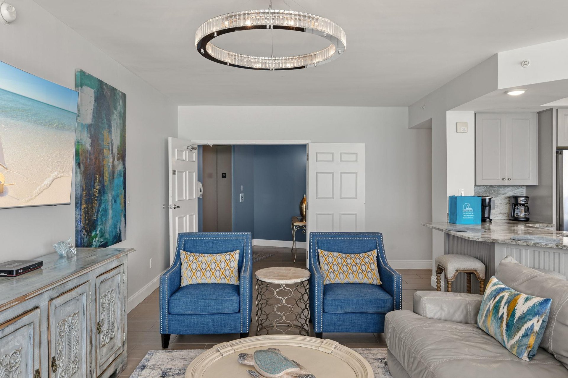 Relax in your sophisticated living space with coastal artwork and stunning chandelier creating perfect ambiance.