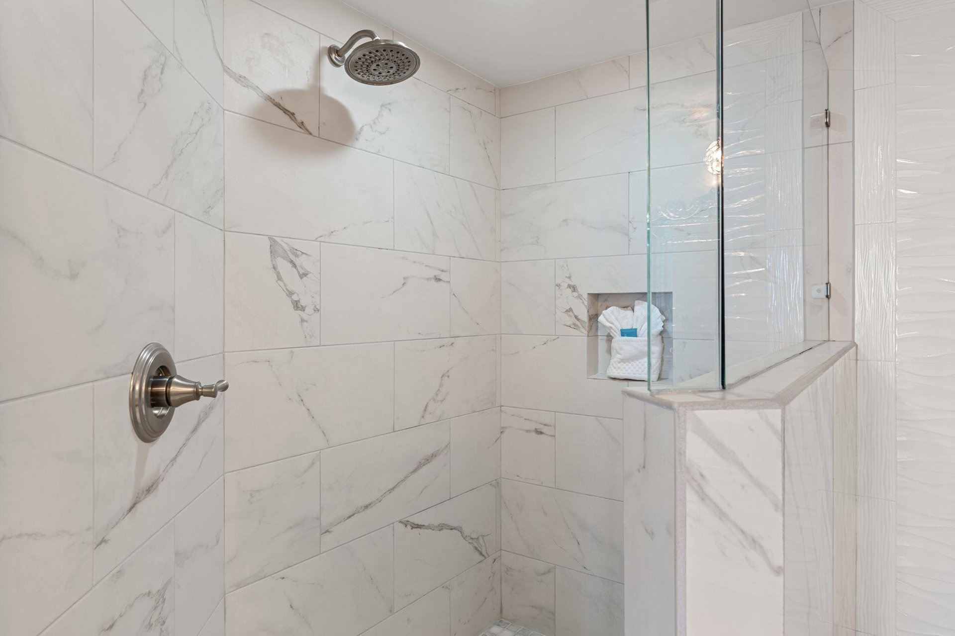 Step into your luxurious marbletiled shower with rainfall showerhead and builtin amenities niche for a spalike experience.