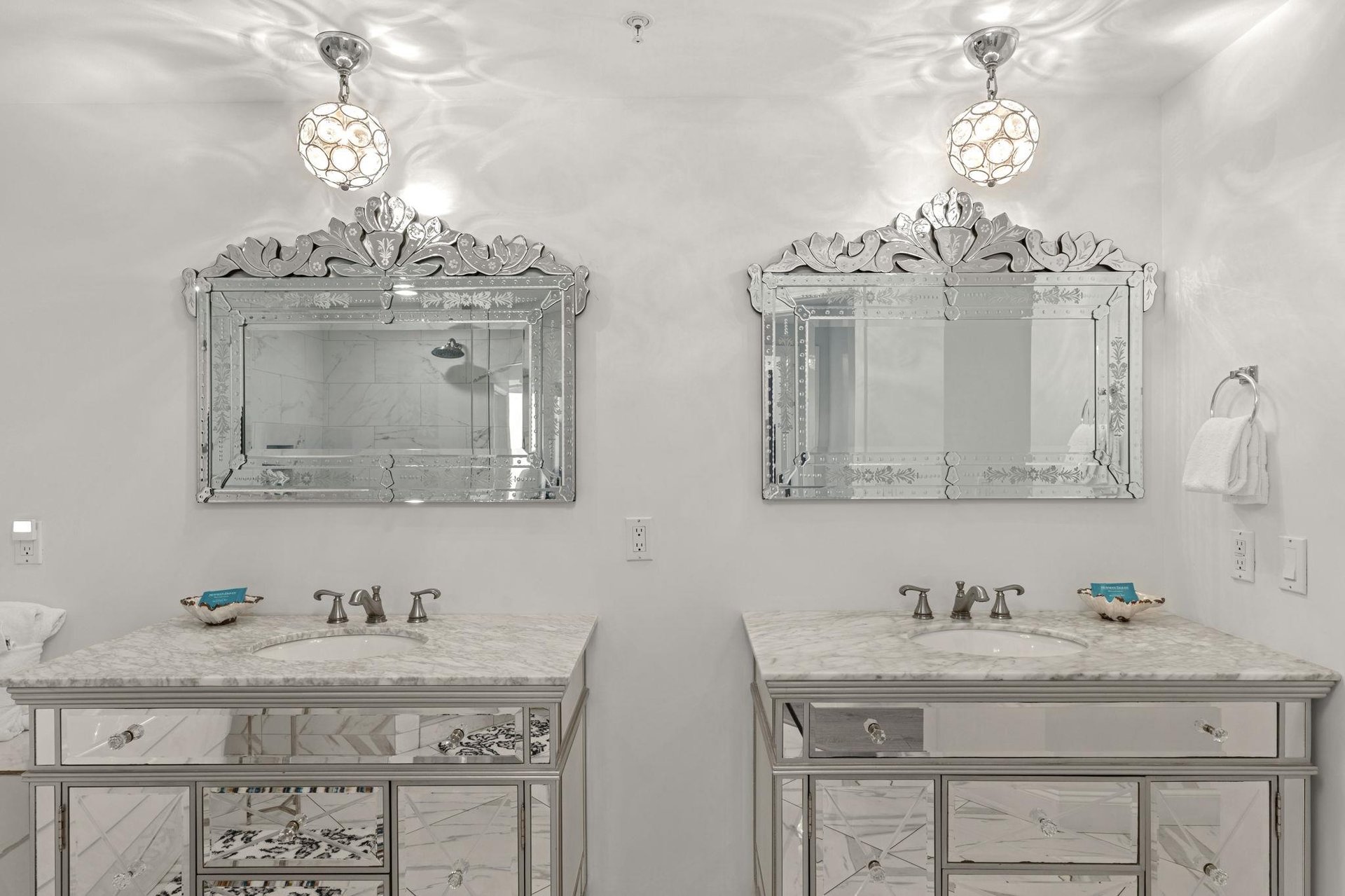 Your luxurious bathroom features dual vanities with Venetian mirrors and sparkling pendant lights, creating an elegant space for your morning routine.